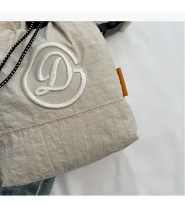 Detail of cream nylon crossbody bag featuring white embroidered D letter and drawstring
