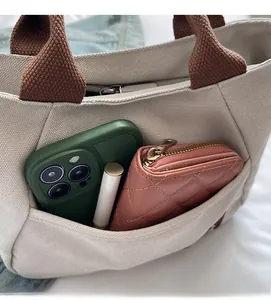 Detail of canvas tote front pocket holding a phone, quilted wallet and lipstick