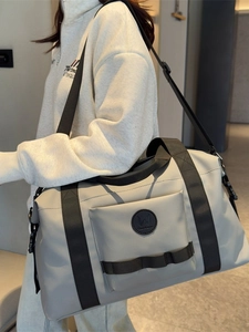 Large beige travel duffel bag with black adjustable shoulder strap and front utility pocket