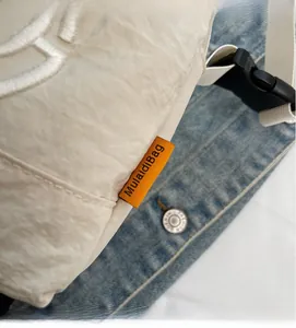 Detailed view of cream pleated crossbody bag with orange woven label and buckle strap