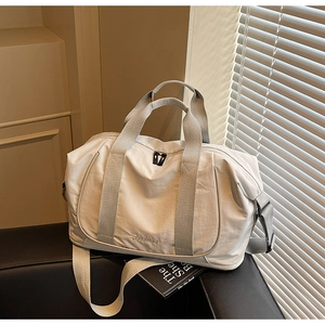 Gros plan d'un sac de voyage crème avec poignées tissées et logo sur canapé en cuir