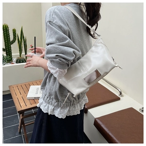 White faux leather shoulder bag with silver metal plaque worn by a model in casual setting