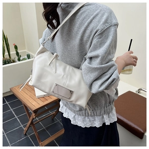 Detail of minimalist cream faux leather crossbody bag with metal plaque and zip tassel