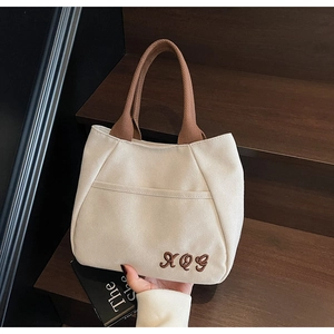 Close-up of off-white canvas tote bag featuring brown embroidered letters and woven handles