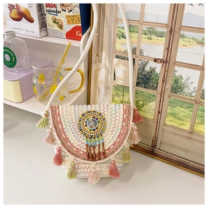 Detail of bohemian straw bag featuring colorful beaded disc and tiered tassel fringe