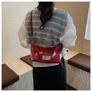 Close-up of shiny red patent leather tote bag with silver metal plaque and slim shoulder strap