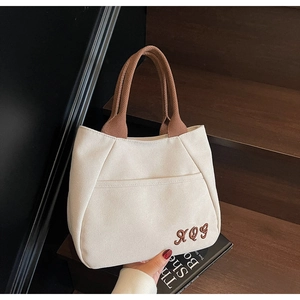 Detailed shot of beige canvas tote bag with brown embroidered letters and woven handles