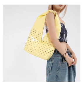 Macro detail of silver studs on a yellow glossy patent leather hobo shoulder bag