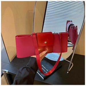 Detail of a bright red leather bow-shaped shoulder bag featuring a golden snap button