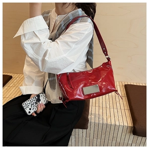 Detail of red patent leather shoulder bag featuring silver metal plate and side zippers