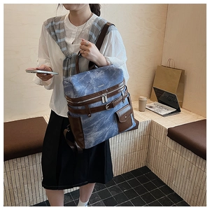 Detail of a large capacity denim blue backpack with brown leather trim and multi-pocket design