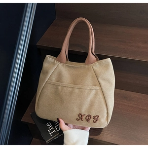 Close-up of khaki canvas tote bag featuring brown woven handle and AQG letter embroidery