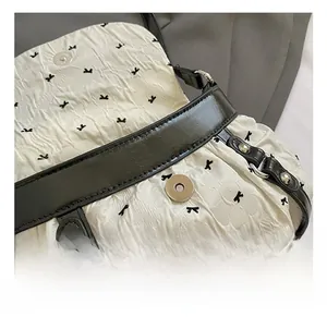 Close-up of white pleated fabric with black bow embroidery and metallic magnetic clasp