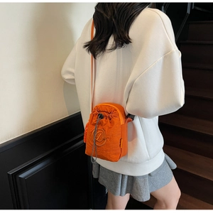 Model wearing orange waterproof nylon crossbody bag with drawstring closure and slim strap