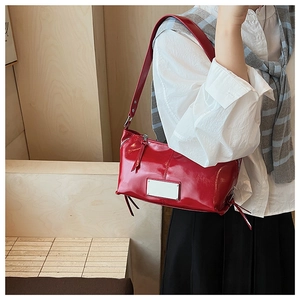 Detail of red glossy shoulder bag with silver metal plaque and chunky strap on model