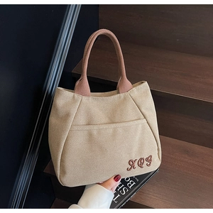 Close-up of beige canvas bucket bag with brown braided handle and RQG letter embroidery