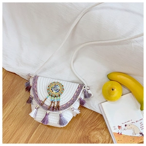 Close-up of woven straw crossbody bag with bohemian tassels and beaded circular pattern