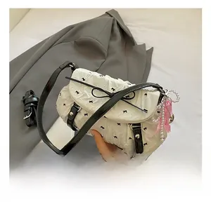 Close-up of white pleated bow bag with pearl charm and ribbon detail on grey blazer