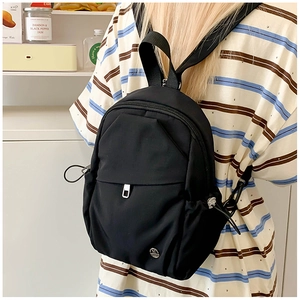 Vue détaillée du mini sac à dos en nylon noir avec poche à rabat et logo en métal rond