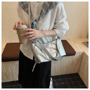 Detail of silver metallic crossbody bag with wide strap and tassel zipper on a white shirt