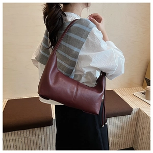 Detail view of burgundy leather shoulder bag with side tassels and sleek vertical stitching