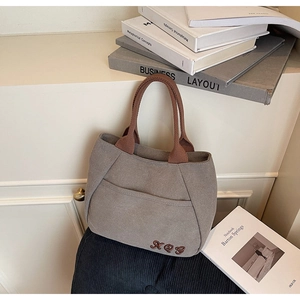 Detail of canvas bucket bag featuring XOQ embroidery and brown woven handle on a shelf