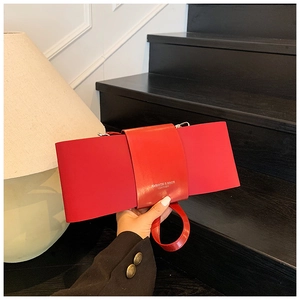 Detail view of a bright red rectangular handbag with a thick strap and a round handle
