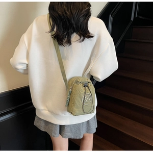 Olive green nylon crossbody bag detail with drawstring pocket shown on a white hoodie