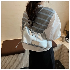 Side view of metallic silver hobo bag on shoulder showing zipper and metal plaque detail