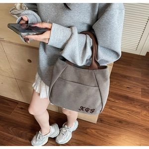Detailed embroidery on grey canvas tote bag with woven handles and front pocket