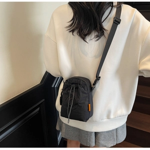 Detail of black nylon drawstring crossbody bag with orange label and adjustable strap
