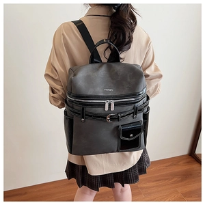 Close-up of grey and black patchwork backpack featuring leather straps and metal buckles