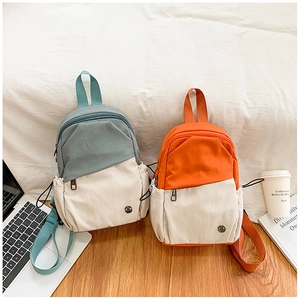Détail de deux mini sacs à dos bicolores en bleu-gris et orange sur un parquet en bois