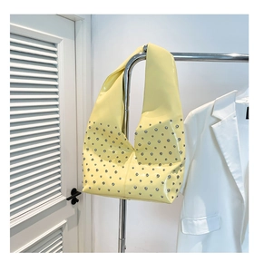 Détail d'un sac hobo en cuir verni jaune avec rivets argentés et finition brillante
