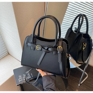 Detail of black faux leather handbag featuring gold buckles and secure zipper closure