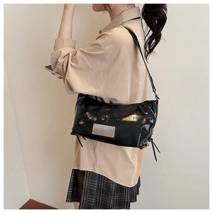 Close-up of a black glossy patent leather shoulder bag with side zipper and metal plaque