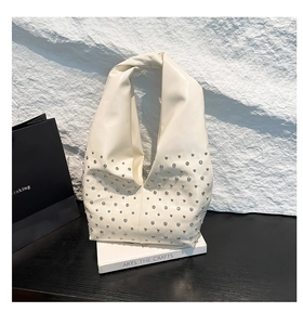 Artistic shot of a beige punk hobo bag with silver rivets on a stone background