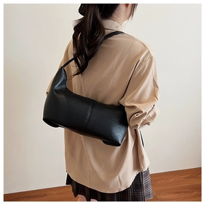 Detail of a minimalist black faux leather shoulder bag worn by a model in a minimal studio