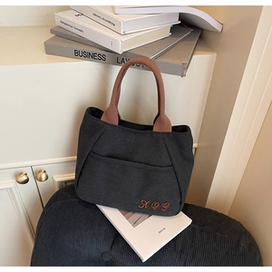 Close-up of durable black canvas tote bag with brown handles and embroidered letters