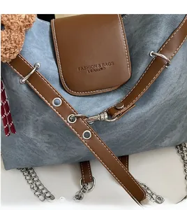 Detail von silbernem Karabinerhaken und Metallkette an Jeans- und Ledertasche