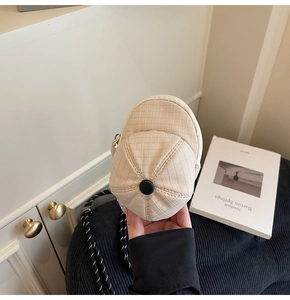Close-up of a beige baseball cap shaped mini coin purse with woven lanyard and zipper detail