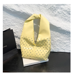 Detail of bright yellow glossy hobo bag with silver rivet studs on white stone background