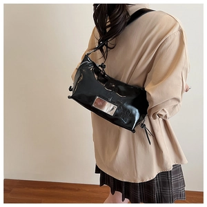 Detail of glossy black patent leather shoulder bag with sleek metal plaque and zip closure
