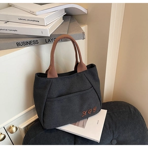 Detailed view of black canvas bucket bag with brown woven handles and embroidered logo