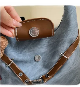 Details zur silbernen Magnetschnalle und weißen Nähten am blauen Denim-Rucksack mit Leder