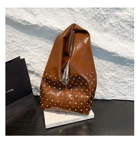 Close-up of brown glossy hobo bag with silver rivet studs on white stone background