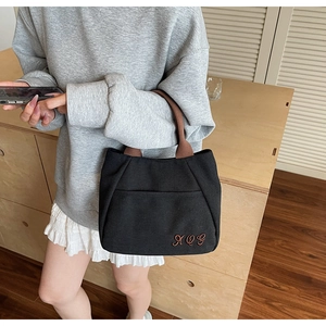 Close-up of black canvas tote bag with brown woven handles and embroidered letter detail