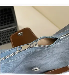 Detailaufnahme des glatten Reißverschlusses an blauer Denim-Tasche mit braunem Lederbesatz