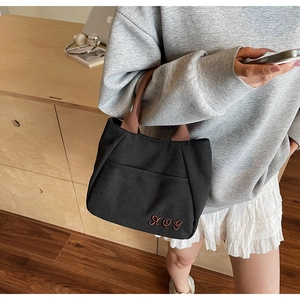 Close-up of black canvas tote bag with brown embroidered AQI letters and side pocket