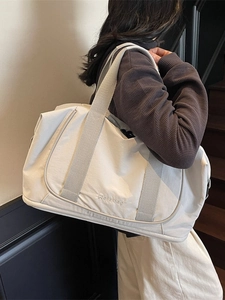 Sac de voyage spacieux blanc cassé avec poignées grises porté par un mannequin en intérieur